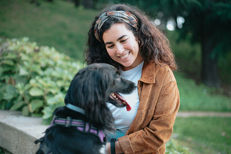 A woman smiling at her black dog while they sit outside